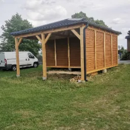 Nowa, drewniana altana z czarnym dachem i rynną, widoczna na trawniku obok białego samochodu dostawczego.