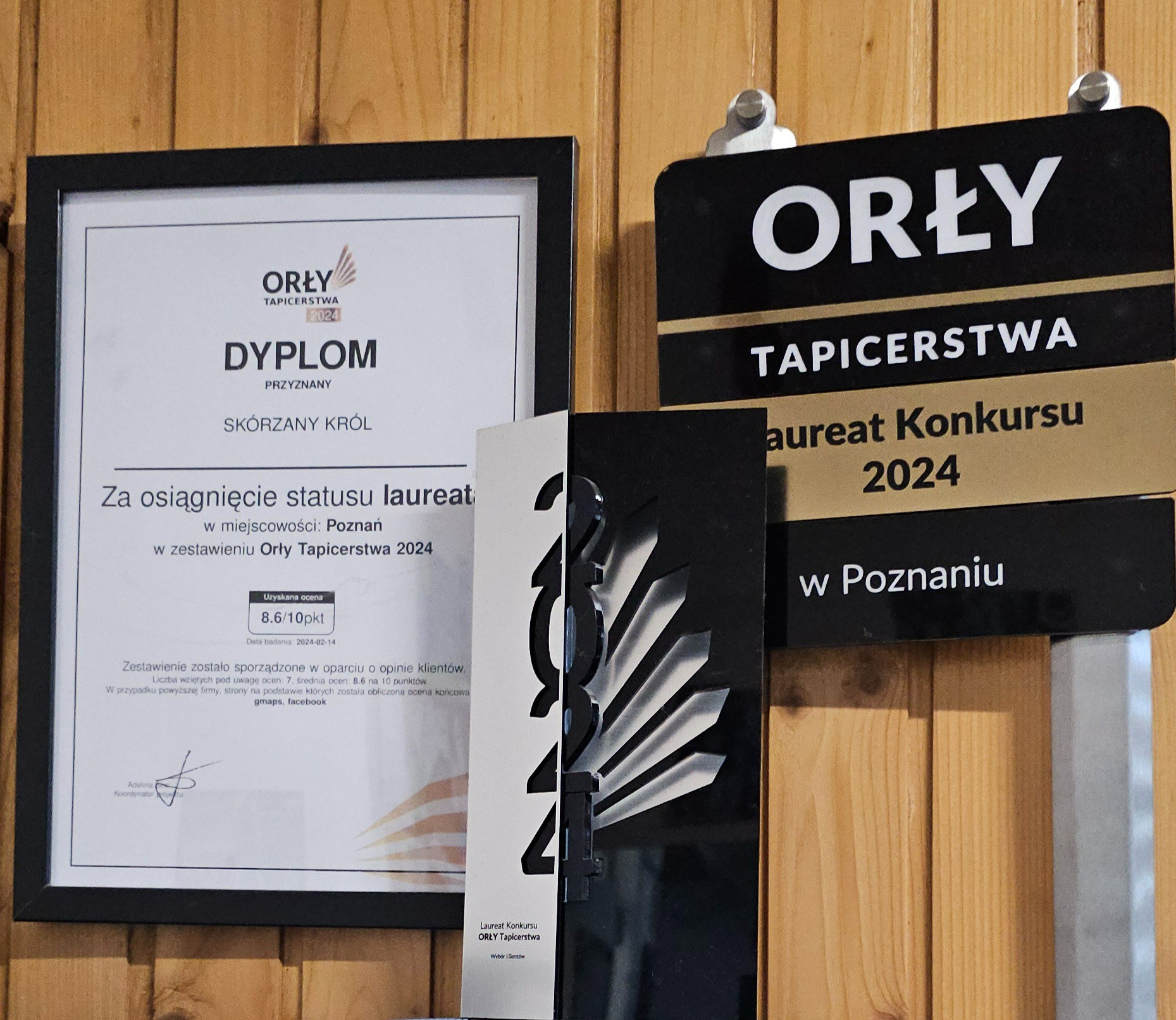 Dyplom i tabliczka z nagrodą 'Orły Tapicerstwa 2024' dla firmy 'Skórzany Król' z Poznania, prezentowane na drewnianej ścianie.