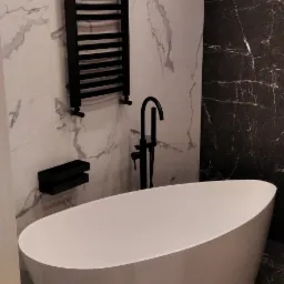 Nowoczesna łazienka z wolnostojącą, owalną wanną, czarną armaturą, grzejnikiem drabinkowym i płytkami imitującymi marmur w dwóch kolorach.