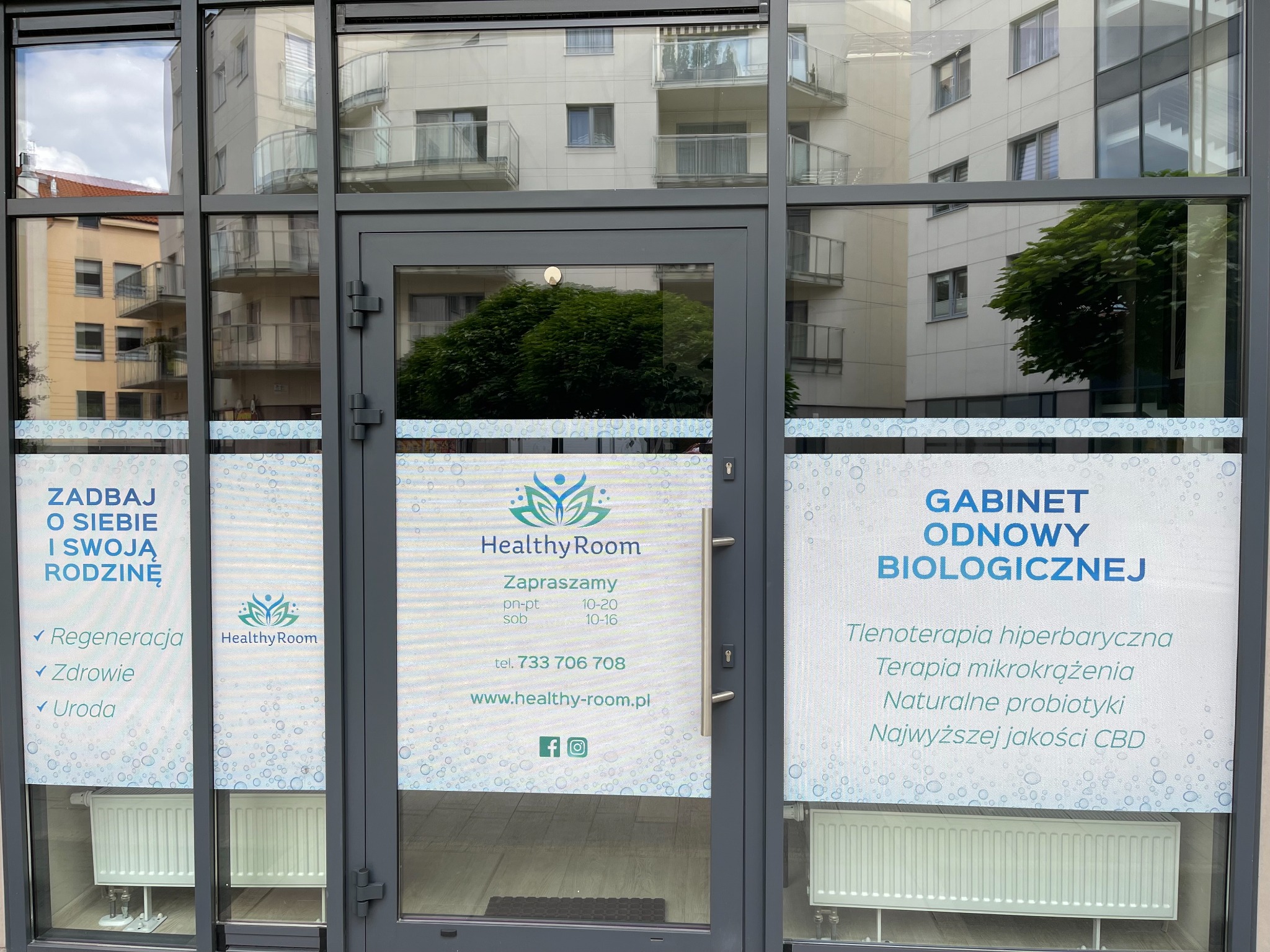 Przeszklone wejście do gabinetu odnowy biologicznej Healthy Room z informacją o regeneracji, zdrowiu, urodzie, tlenoterapii hiperbarycznej, terapii mikrokrążenia, naturalnych probiotykach i CBD.