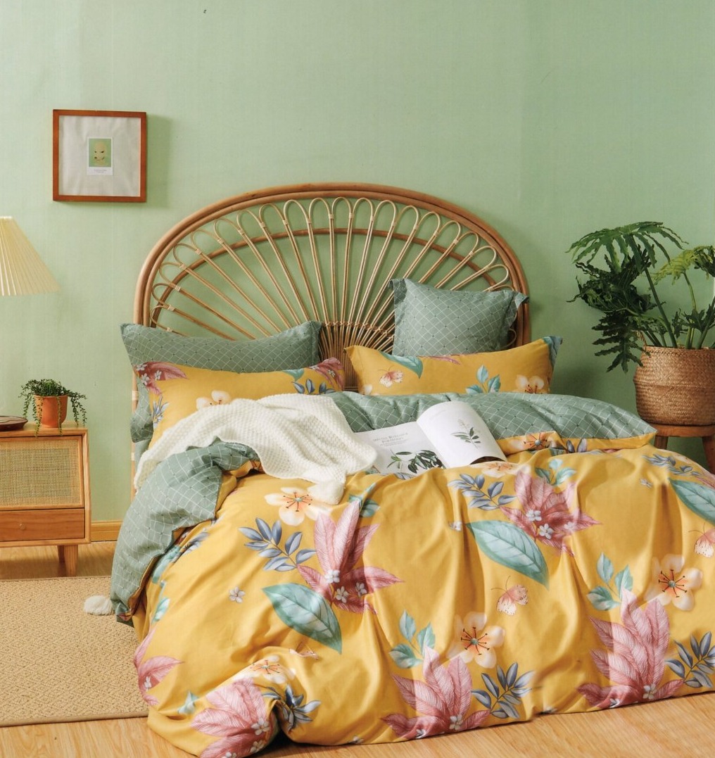 Ustawione łóżko z pościelą w kwiatowy wzór na żółtym tle, z rattanowym zagłówkiem, w tle zielona ściana i roślina w wiklinowym koszu.