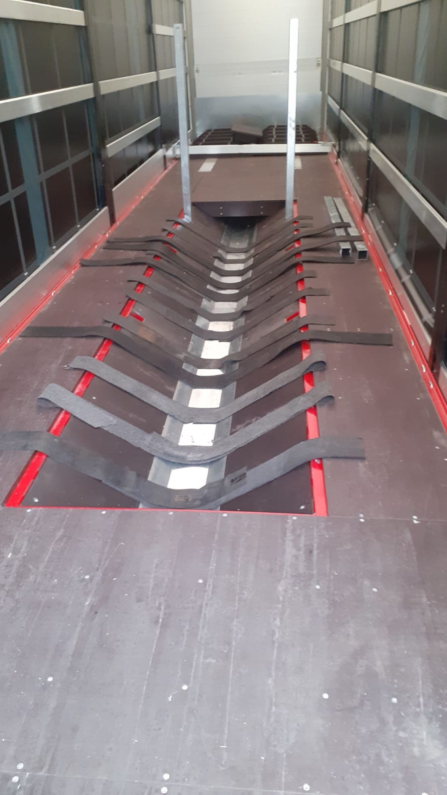 Wnętrze pustej naczepy z zamocowanymi pasami zabezpieczającymi ładunek na podłodze i metalowymi elementami mocującymi w górnej części.