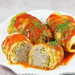 Gołąbki polane sosem pomidorowym i udekorowane koperkiem, przygotowane na catering we Wrocławiu, widoczne na białym talerzu.