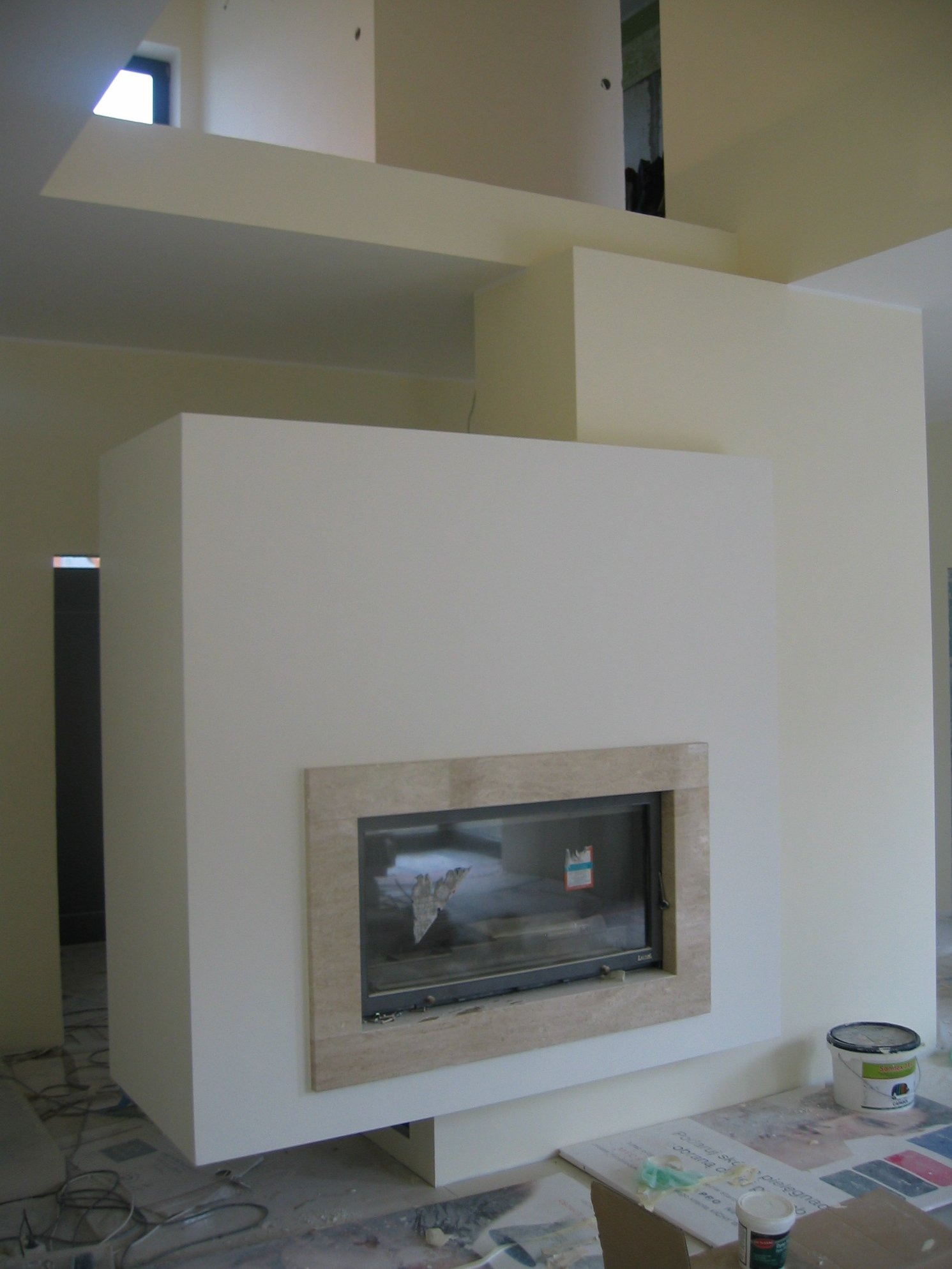 Wnęka kominkowa obudowana płytami gipsowymi, z marmurowym obramowaniem, w trakcie prac wykończeniowych, widoczne kable na podłodze i puszka farby.