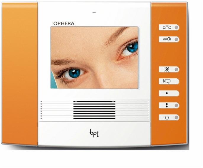 Panel wideodomofonu marki BPT Ophera z widocznym ekranem wyświetlającym zbliżenie na niebieskie oczy osoby, z pomarańczowymi elementami obudowy i białym tłem.