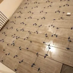 Układanie podłogi z płytek imitujących drewno z użyciem krzyżyków dystansowych, widoczny fragment nieukończonej posadzki.