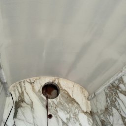 Lukasz Witek - Fragment sufitu i ściany wykończonej marmurem z widocznym otworem na instalację elektryczną i wystającymi przewodami.