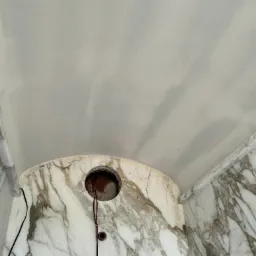 Fragment sufitu i ściany wykończonej marmurem z widocznym otworem na instalację elektryczną i wystającymi przewodami.