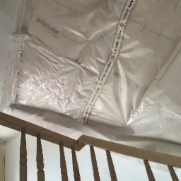 Folia paroizolacyjna Isover Vario KB 1 zabezpiecza sufit podczas prac remontowych, widoczna drewniana balustrada schodów i fragment drabiny.