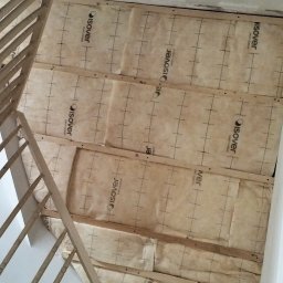 Lukasz Witek - Przygotowanie ściany pod schodami: izolacja z wełny mineralnej Isover zamocowana do drewnianej konstrukcji szkieletowej, widok z dołu.