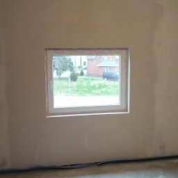 Lukasz Witek - Wnętrze pokoju w Dębnie przed wykończeniem: ściany po szpachlowaniu, z widocznym oknem i surową podłogą, przygotowane do dalszych prac remontowych.