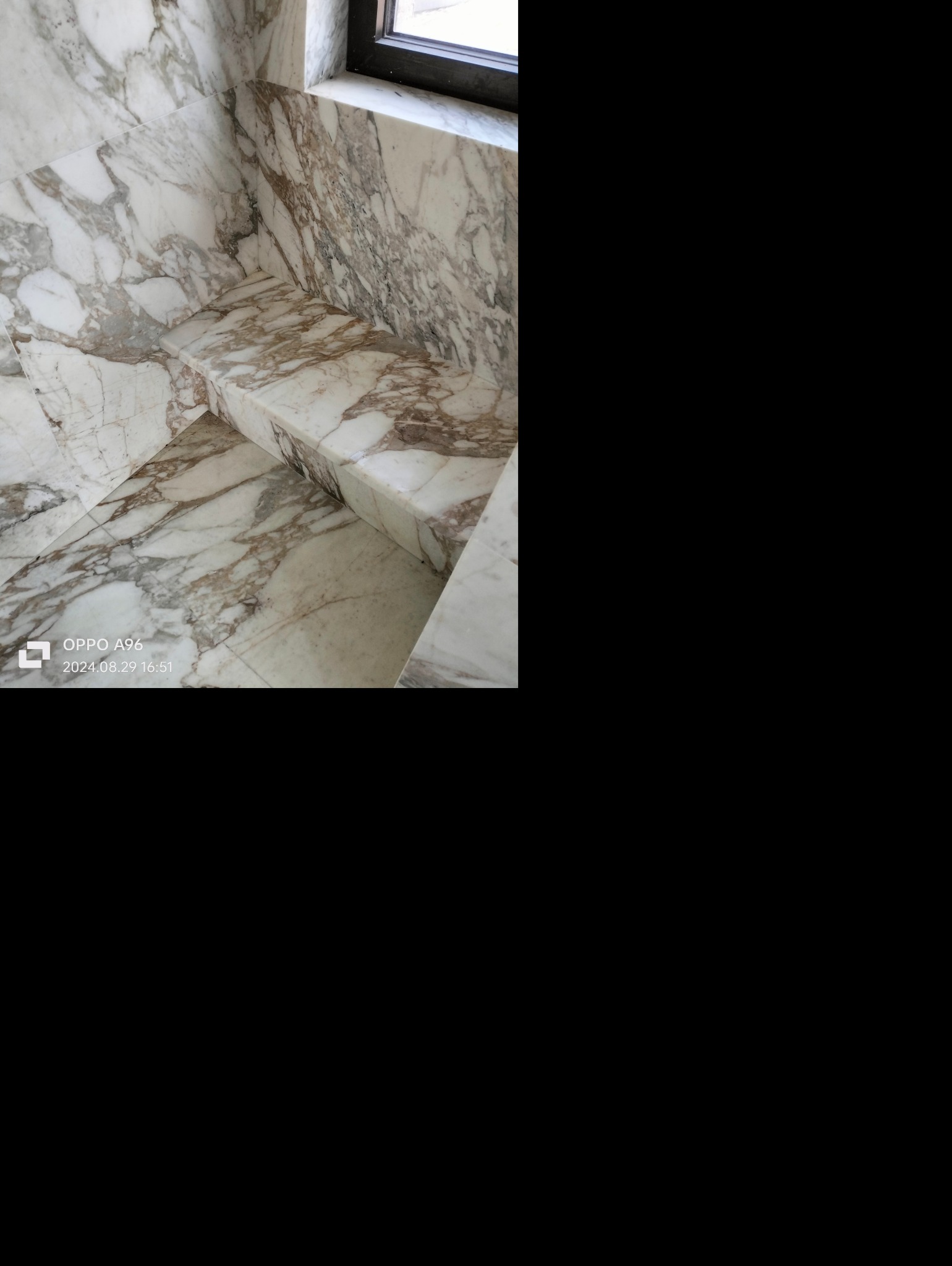 Fragment łazienki wyłożony białym marmurem z brązowymi żyłkami, widoczny parapet okienny i półka z tego samego materiału, ujęcie z dołu.