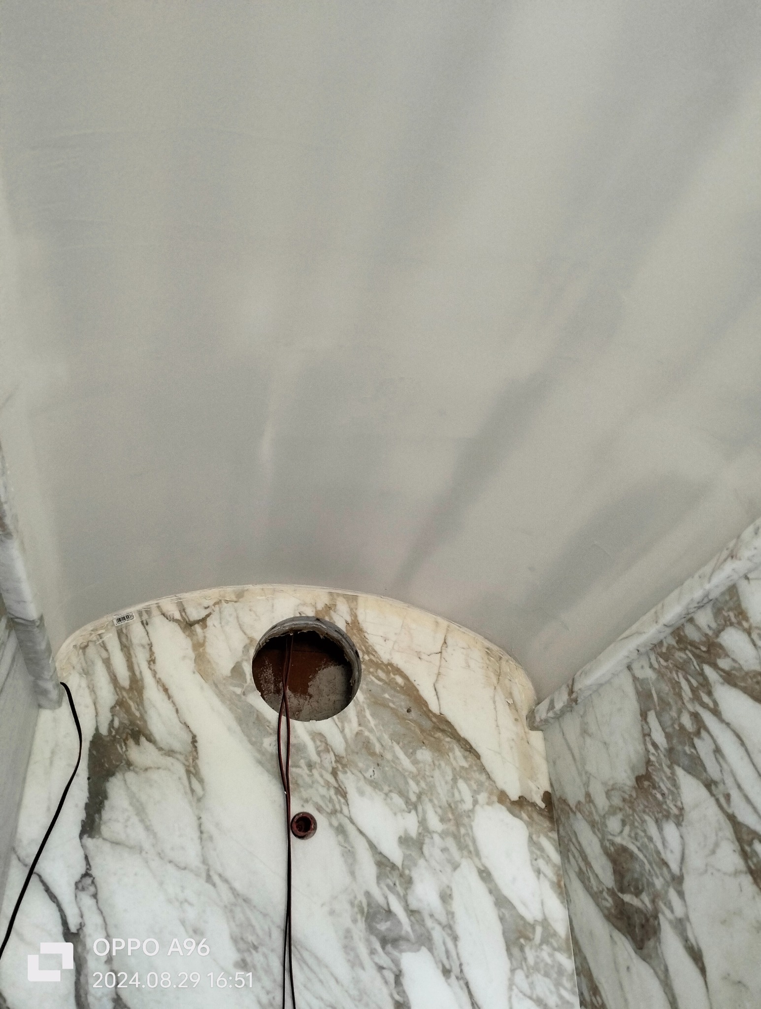 Fragment sufitu i ściany wykończonej marmurem z widocznym otworem na instalację elektryczną i wystającymi przewodami.