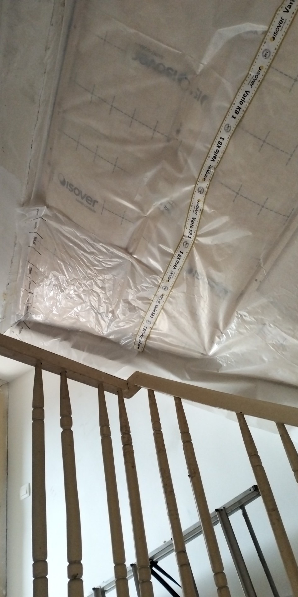 Folia paroizolacyjna Isover Vario KB 1 zabezpiecza sufit podczas prac remontowych, widoczna drewniana balustrada schodów i fragment drabiny.