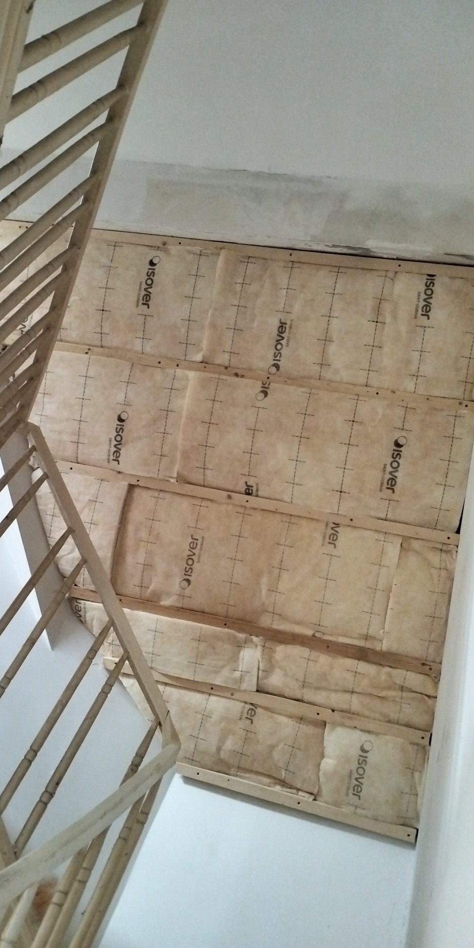 Przygotowanie ściany pod schodami: izolacja z wełny mineralnej Isover zamocowana do drewnianej konstrukcji szkieletowej, widok z dołu.