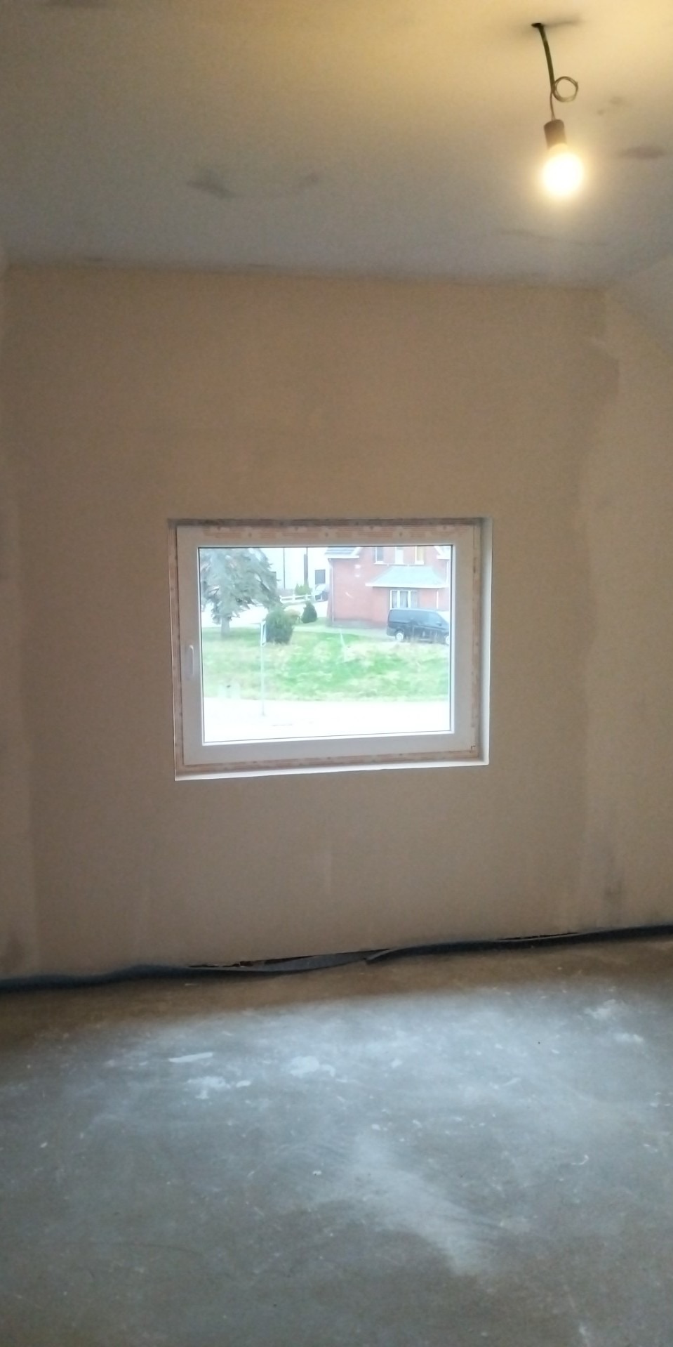 Wnętrze pokoju w Dębnie przed wykończeniem: ściany po szpachlowaniu, z widocznym oknem i surową podłogą, przygotowane do dalszych prac remontowych.