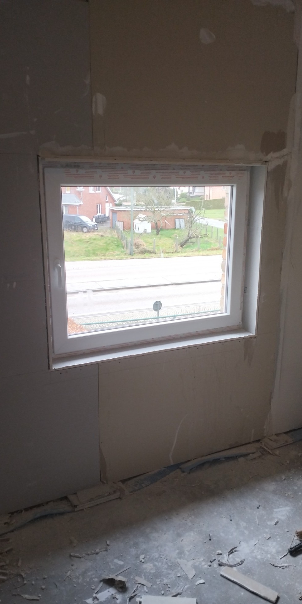 Przygotowanie ściany z płyt gipsowo-kartonowych wokół okna, widoczne łączenia płyt wymagające szpachlowania, fragment podłogi z resztkami materiałów budowlanych.