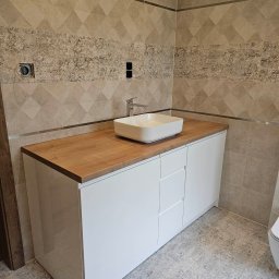 Lili Meble - Ireneusz Figiel - Łazienka z białą szafką umywalkową z drewnianym blatem, kwadratowa umywalka nablatowa i beżowe płytki na ścianach.