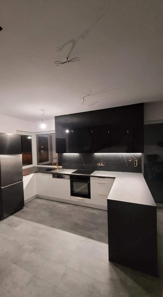 Nowoczesna kuchnia z czarnymi, lakierowanymi szafkami górnymi i białymi szafkami dolnymi, oświetleniem LED pod szafkami, widoczne niedokończone instalacje elektryczne na suficie.