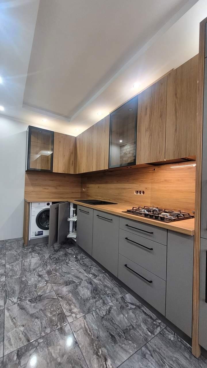 Szara kuchnia z drewnianymi akcentami, zabudowana pralka i szafka cargo, marmurowe płytki na podłodze.