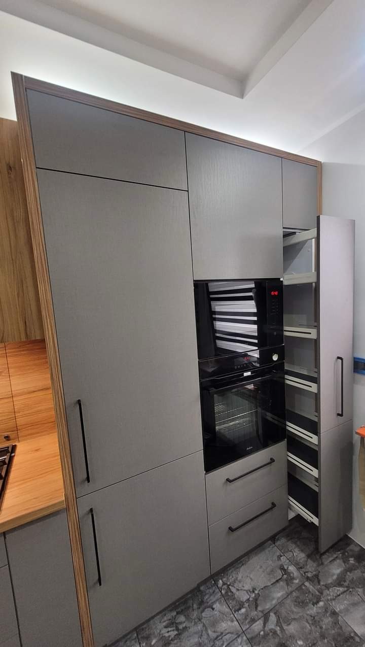 Nowoczesna zabudowa kuchenna w odcieniach szarości z drewnianymi akcentami, piekarnikiem w zabudowie i wysuwaną szafką cargo, oświetlenie LED podszafkowe.