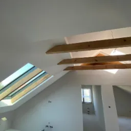 Poddasze w Warszawie po ociepleniu, widoczne drewniane belki i okno dachowe, ściany przygotowane do malowania.