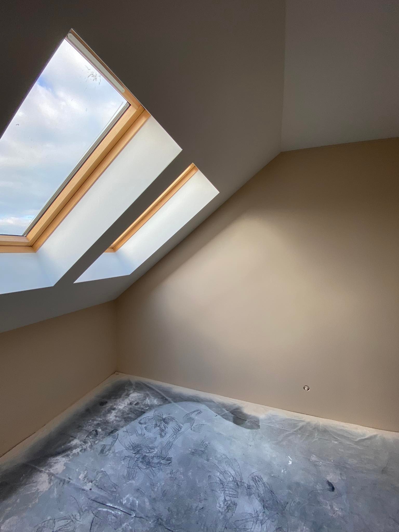 Poddasze po malowaniu na beżowo, z oknami dachowymi i folią ochronną na podłodze.