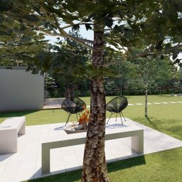Prrfect Place - pracownia projektowanua wnętrz i ogrodów - Natalia Pająk - Nowoczesny ogród z paleniskiem otoczonym białymi ławkami i czarnymi krzesłami, widok przez pień drzewa.