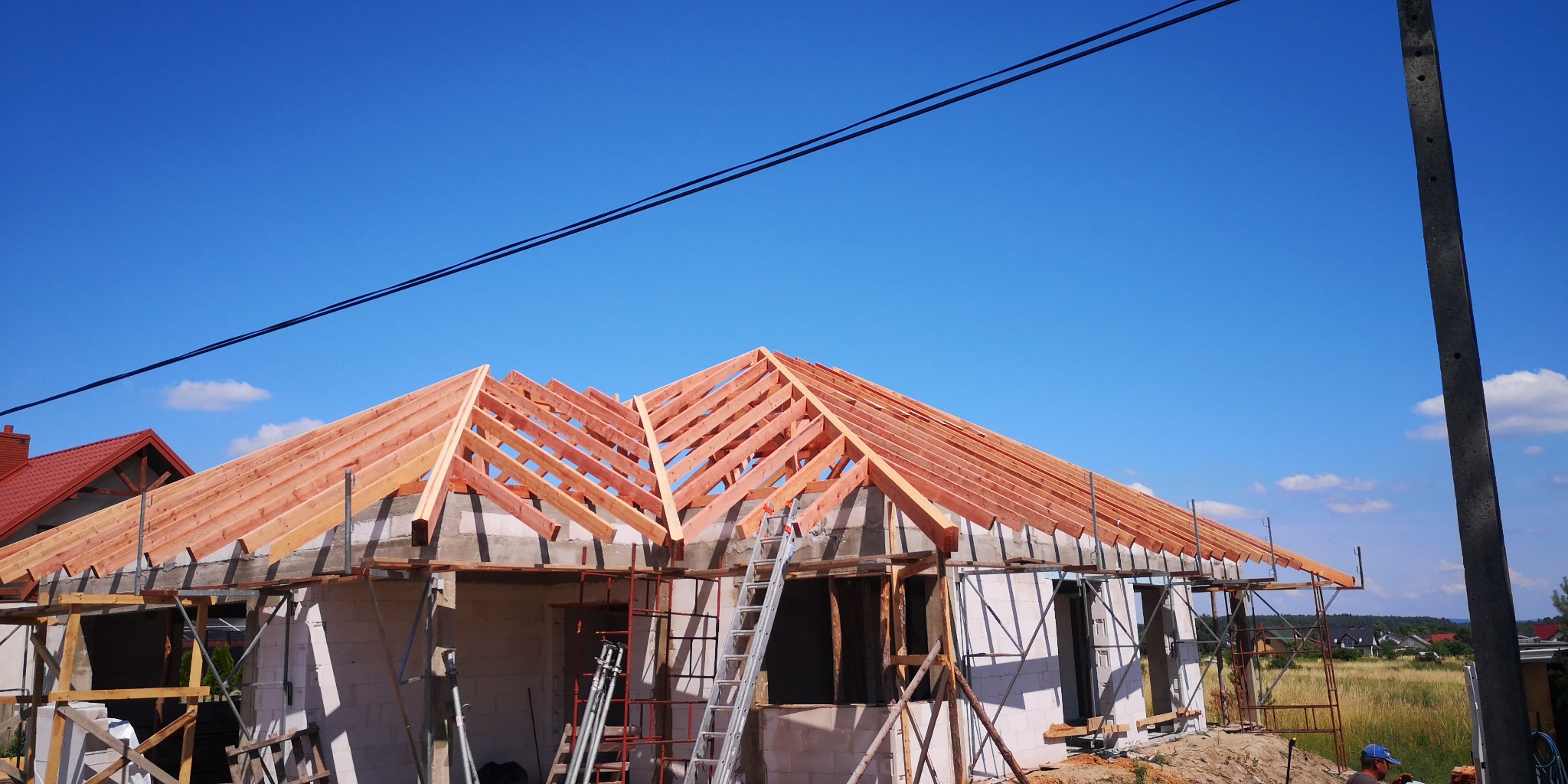 Więźba dachowa z drewna na budowie domu jednorodzinnego w Jędrzejowie, widoczna drabina i rusztowania.