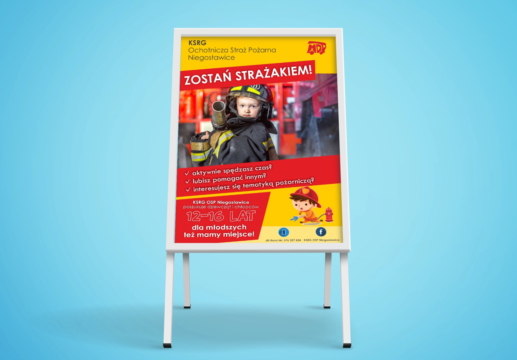 Plakat reklamowy na stojaku, zachęcający do wstąpienia do Ochotniczej Straży Pożarnej w Niegosławicach, z wizerunkiem dziecka w hełmie strażackim i hasłem 'Zostań Strażakiem!'.