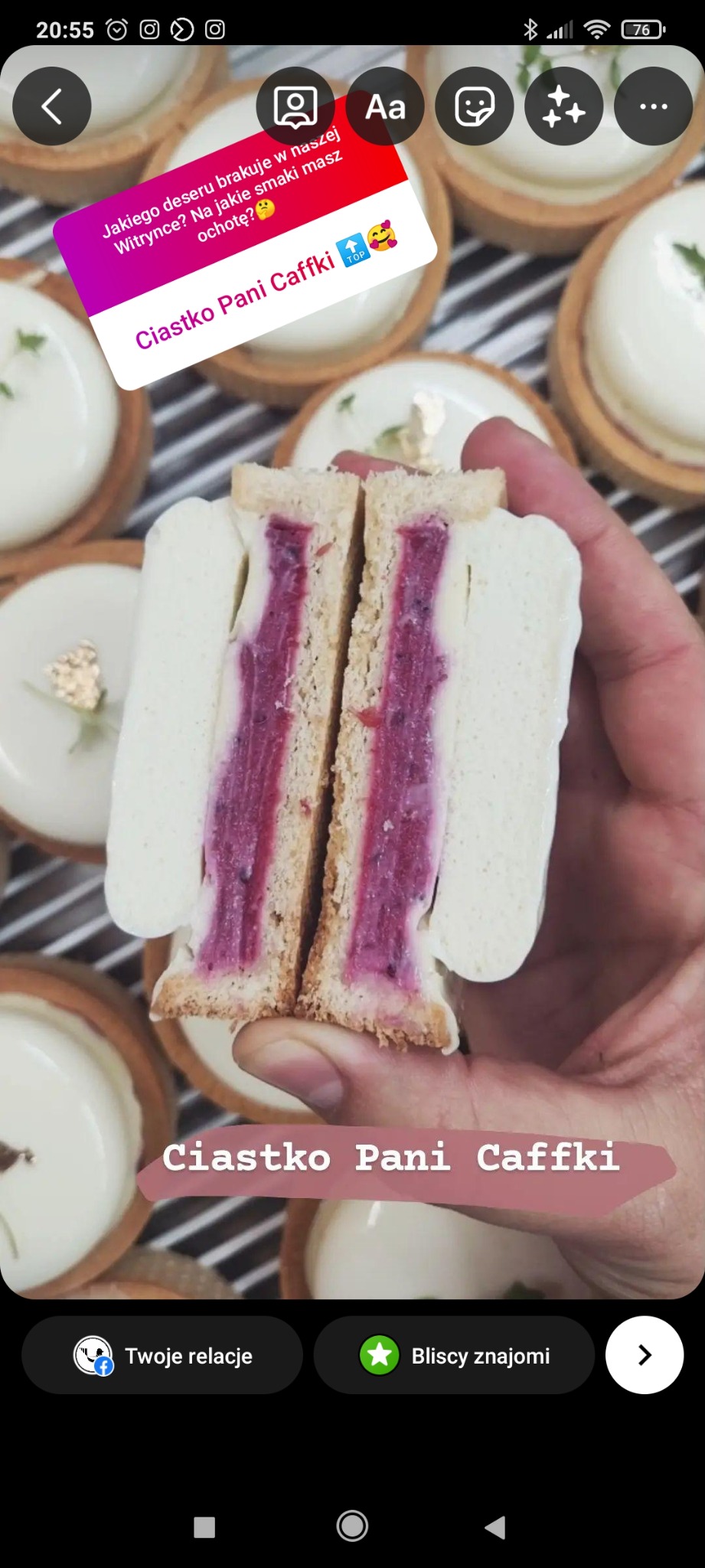 Przekrojone na pół ciastko z białym kremem i fioletowym nadzieniem trzymane w dłoni, w tle widoczne inne ciastka z białym kremem i złotymi listkami.