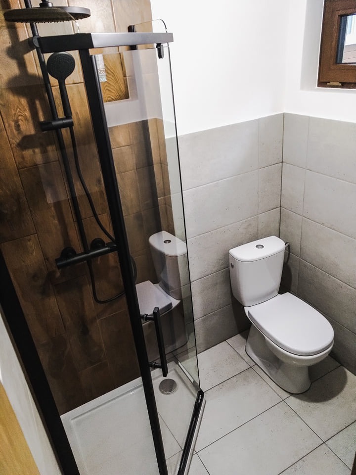 Nowoczesna łazienka z kabiną prysznicową typu walk-in z czarnymi elementami, drewnopodobnymi płytkami w strefie prysznica oraz wiszącą toaletą.