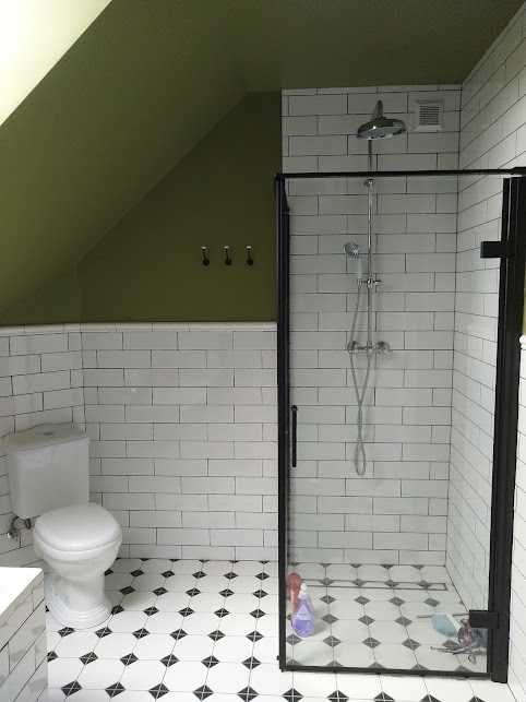 Ukończona łazienka na poddaszu z białymi kaflami, czarnymi fugami, podłogą w biało-czarne romby i kabiną prysznicową z czarną ramą.