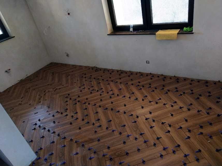 Układanie parkietu w jodełkę z użyciem klipsów poziomujących w pokoju z oknem dachowym, widoczne niedoskonałości ścian.