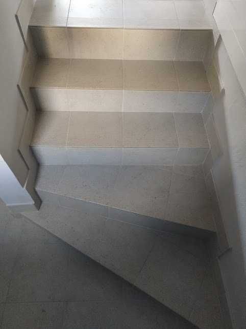 Wykończone schody wewnętrzne z płytek ceramicznych w odcieniach beżu i szarości, widok z góry.