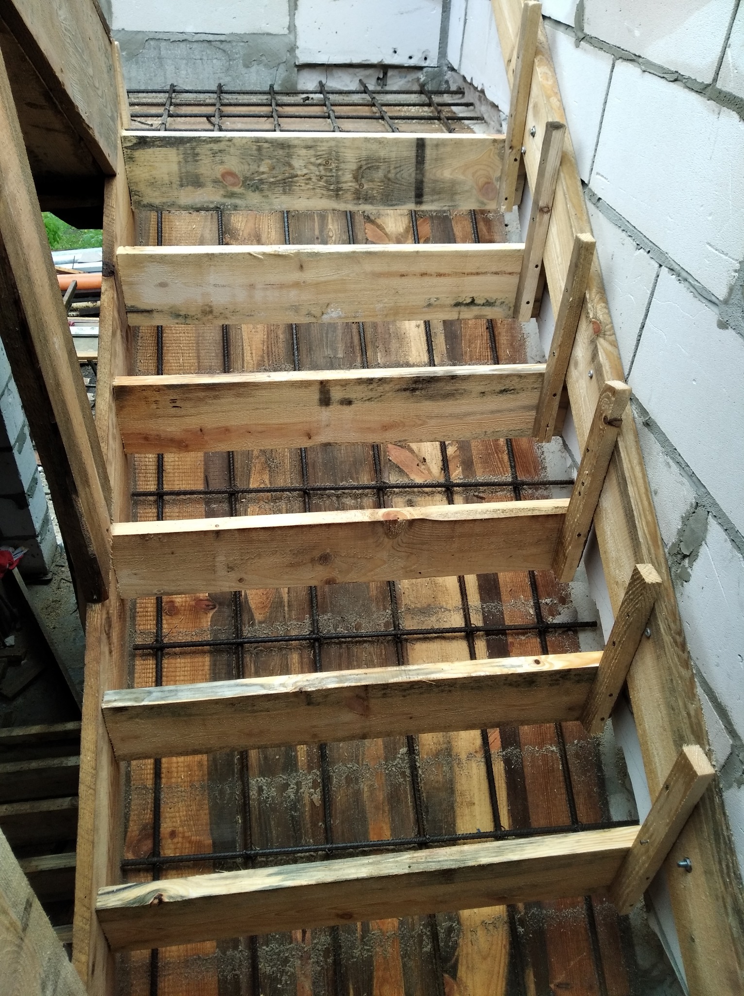 Konstrukcja drewniana szalunku schodów zbrojonych, widok z góry, surowe drewno, bloczki betonowe w tle.