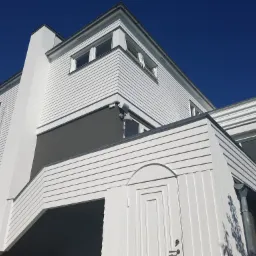 Nowoczesny dom z białymi drewnianymi panelami, szarą wstawką i ciemnym podcieniem, widziany z dołu pod ostrym kątem w słoneczny dzień.