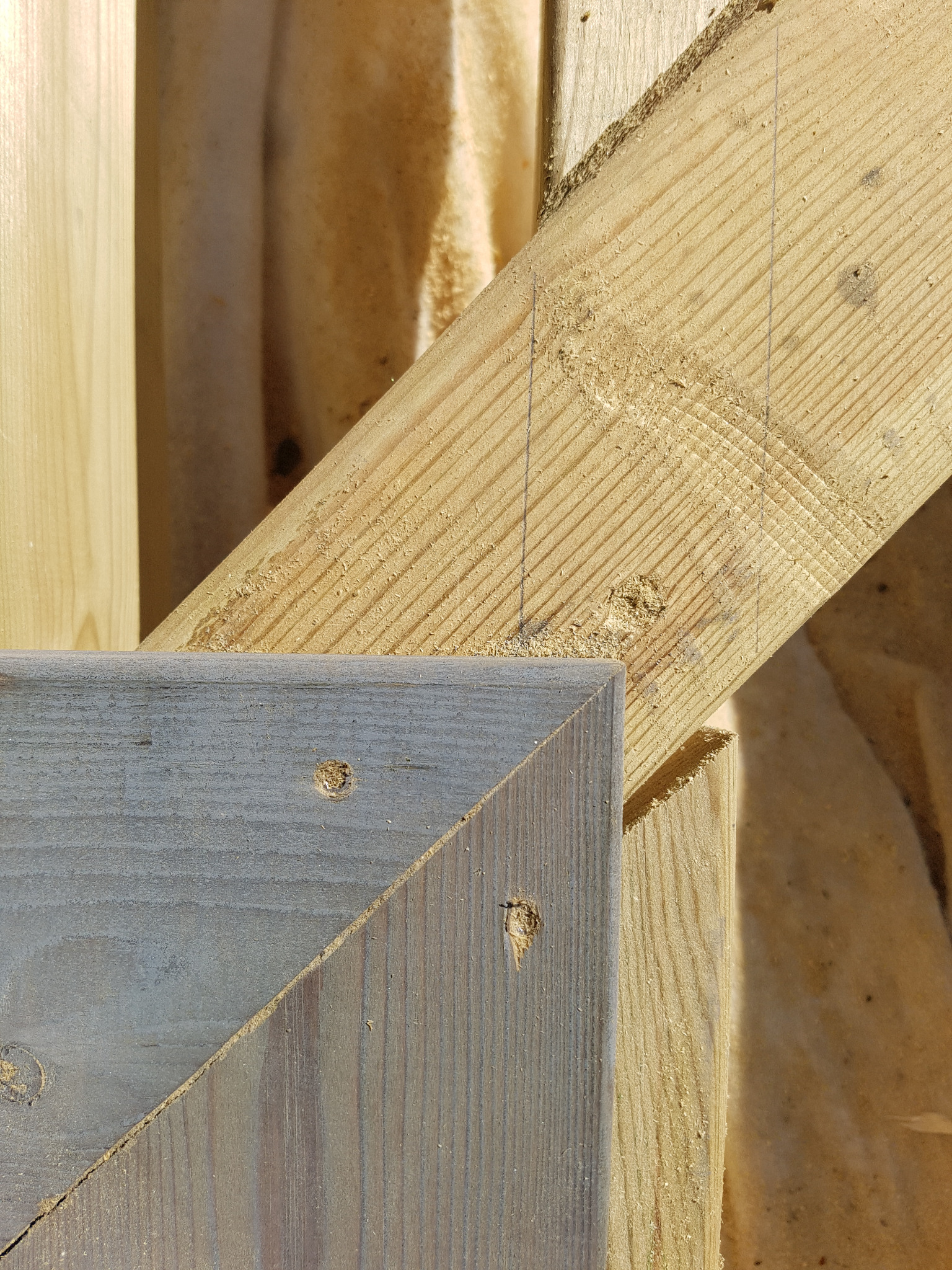 Fragment konstrukcji drewnianej z widocznymi elementami z surowego drewna i szarej bejcy, z bliska, z widocznymi śladami obróbki i liniami pomocniczymi.