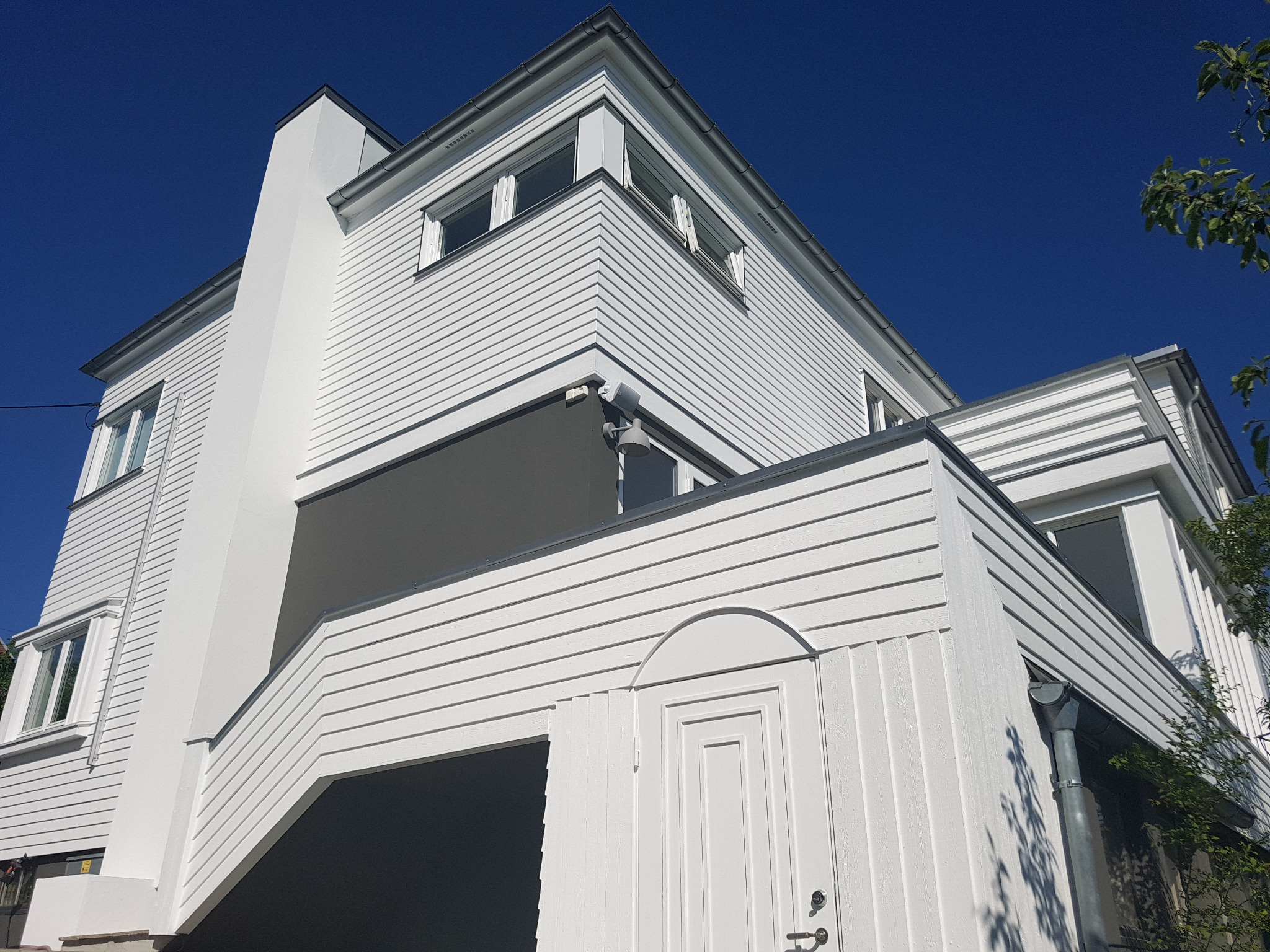 Nowoczesny dom z białymi drewnianymi panelami, szarą wstawką i ciemnym podcieniem, widziany z dołu pod ostrym kątem w słoneczny dzień.