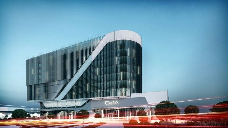 Nowoczesny budynek biurowy z przeszkloną fasadą, z napisem 'Business Center' i 'Cafe' nad wejściem, uchwycony z perspektywy ulicy z rozmazanymi światłami przejeżdżających samochodów.