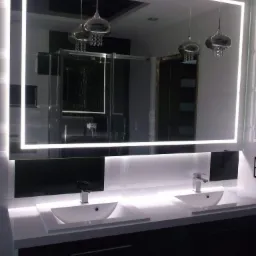 Nowoczesna łazienka z podwójną umywalką nablatową, lustrem z podświetleniem LED i designerskimi lampami wiszącymi z elementami kryształowymi, odbijającymi się w lustrze.