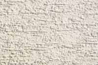 Jasna, kremowa elewacja o wyraźnej, poziomej fakturze baranka, wykonana z bliska, ukazująca nierówności i strukturę tynku.