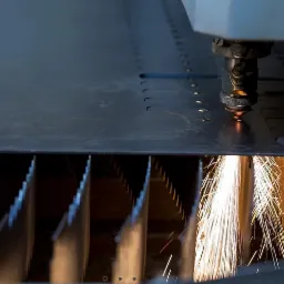 Proces cięcia metalu laserem, widoczne iskry i precyzyjne wycinanie otworów w arkuszu blachy.