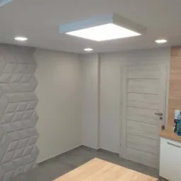 Nowoczesne wnętrze z dekoracyjną ścianą z paneli 3D, drewnianym blatem i kwadratową lampą sufitową LED.