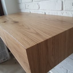 STOL-Design - Półka z drewna dębowego z szufladami, zamontowana na ścianie z białej cegły, widok z dołu, na podłodze folia malarska i worek z zaprawą.