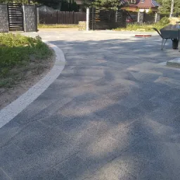 Ułożona kostka brukowa na podjeździe w Białymstoku, widoczna brama wjazdowa i dom w tle, taczka z piaskiem obok.