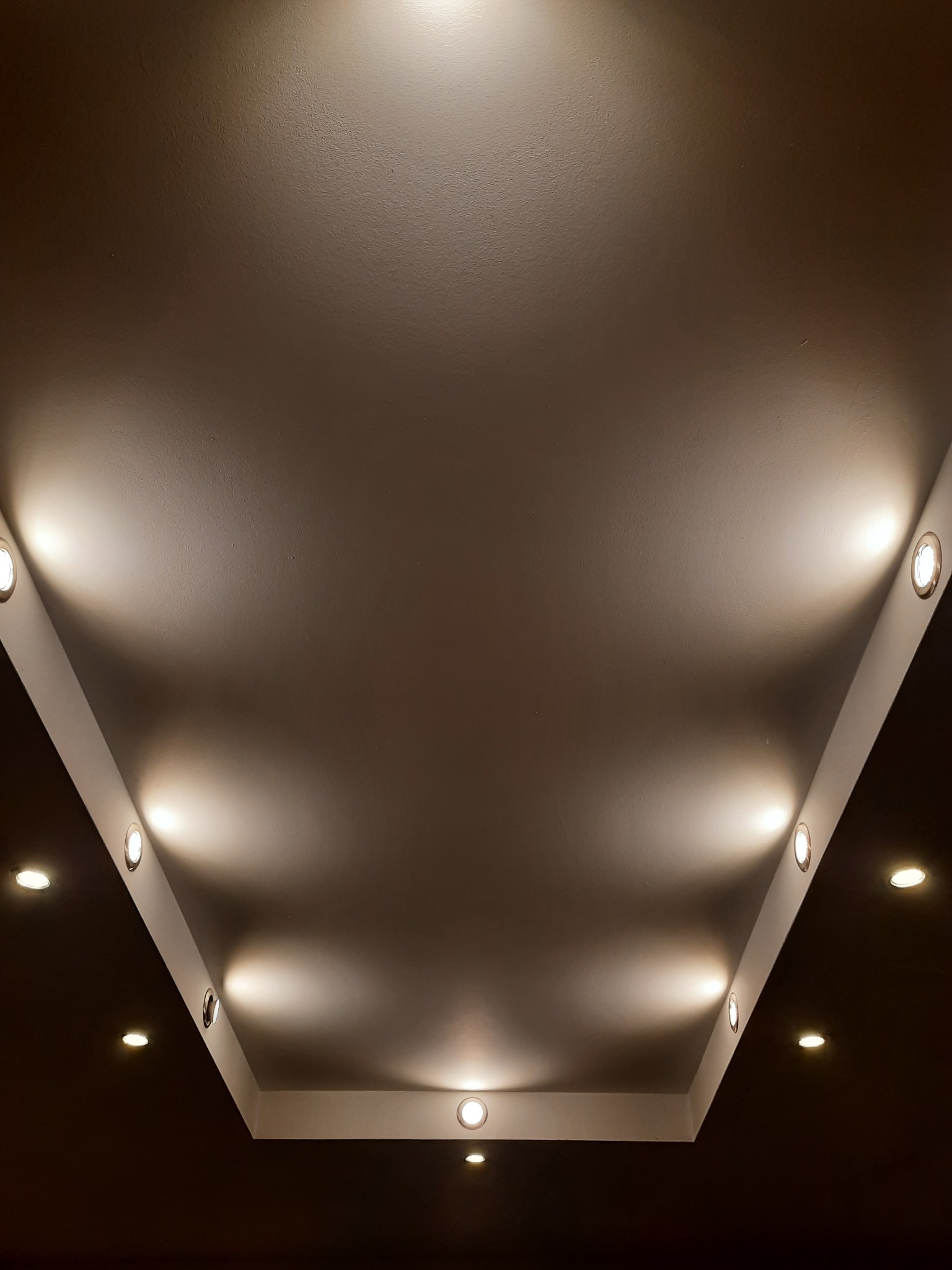 Sufit podwieszany z oświetleniem punktowym, rozmieszczonym wzdłuż krawędzi obniżonej części sufitu, tworzącej geometryczny wzór.