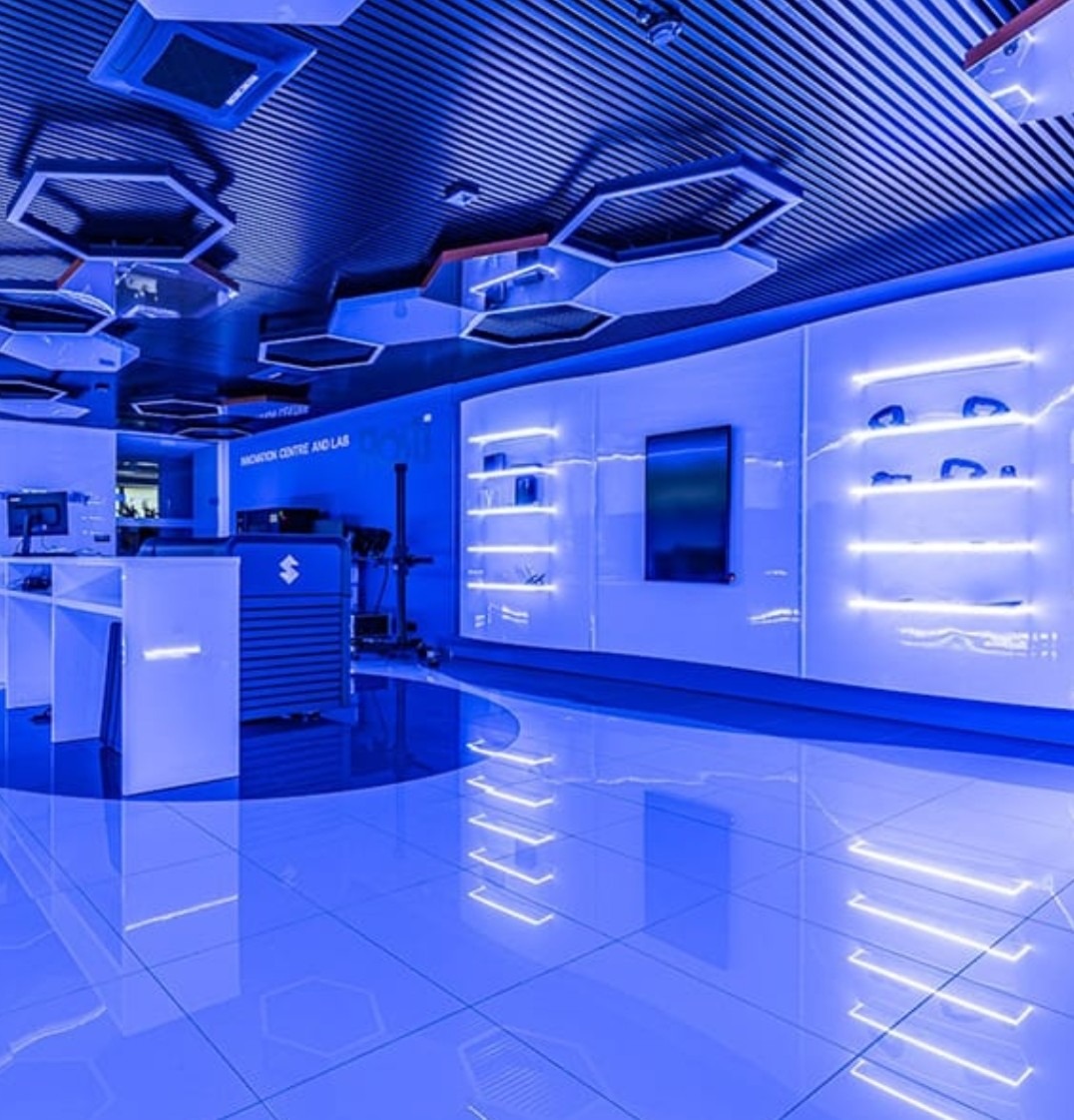 Nowoczesne wnętrze biurowe z podświetlonymi regałami, błyszczącą podłogą i dekoracyjnymi panelami sufitowymi w odcieniach niebieskiego.