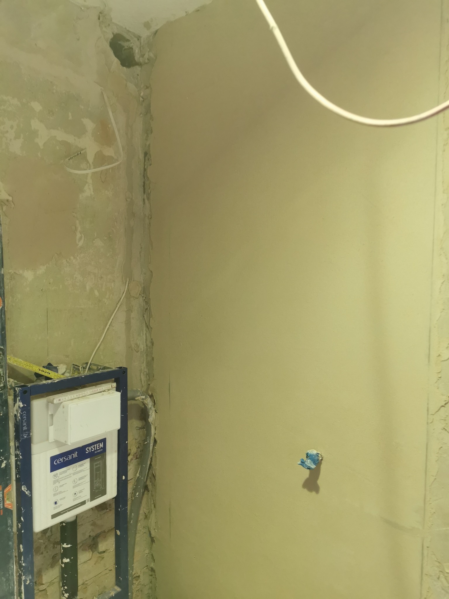 Montaż stelaża podtynkowego WC Cersanit System w surowym stanie łazienki, widoczne ślady po skuciu tynku i wystające przewody elektryczne.