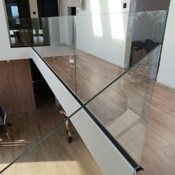 MS-PRO Marek Szczepanek - Szklana balustrada na antresoli z drewnianą podłogą, widoczne ślady montażu i częściowo wykończone ściany.